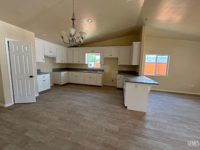 kitchen featuring a chandelier, a sink, white cabinets, a peninsula, and lofted ceiling