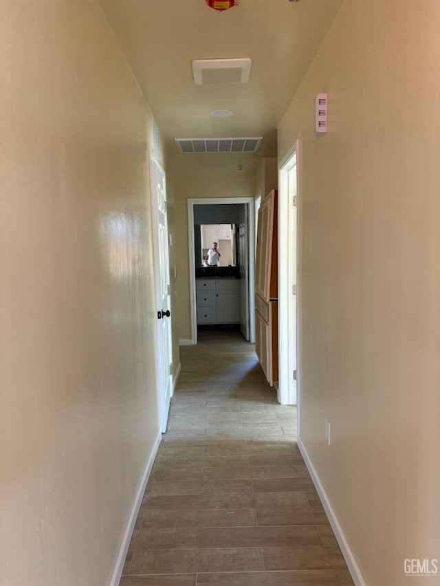 corridor with baseboards, wood finished floors, and visible vents