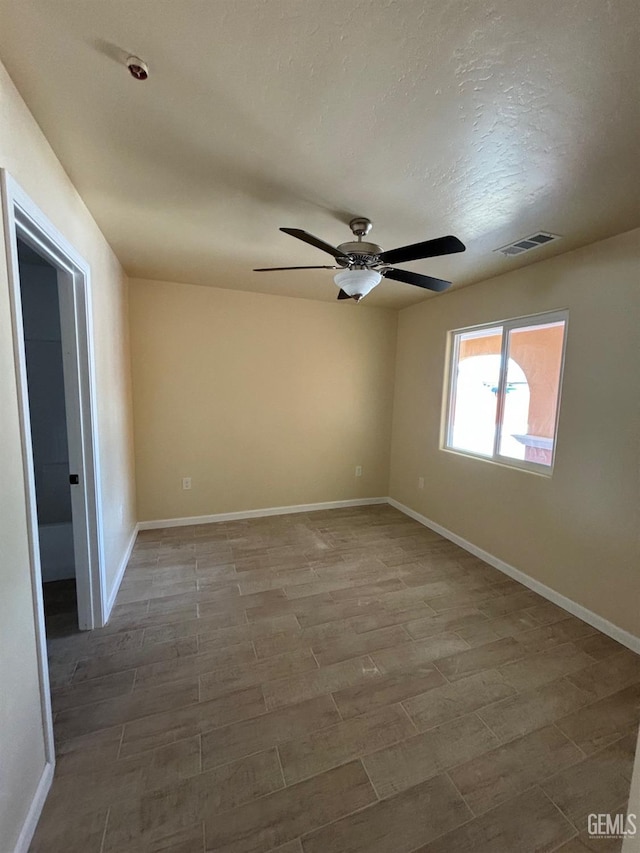 unfurnished room with a textured ceiling, a ceiling fan, baseboards, wood finished floors, and visible vents