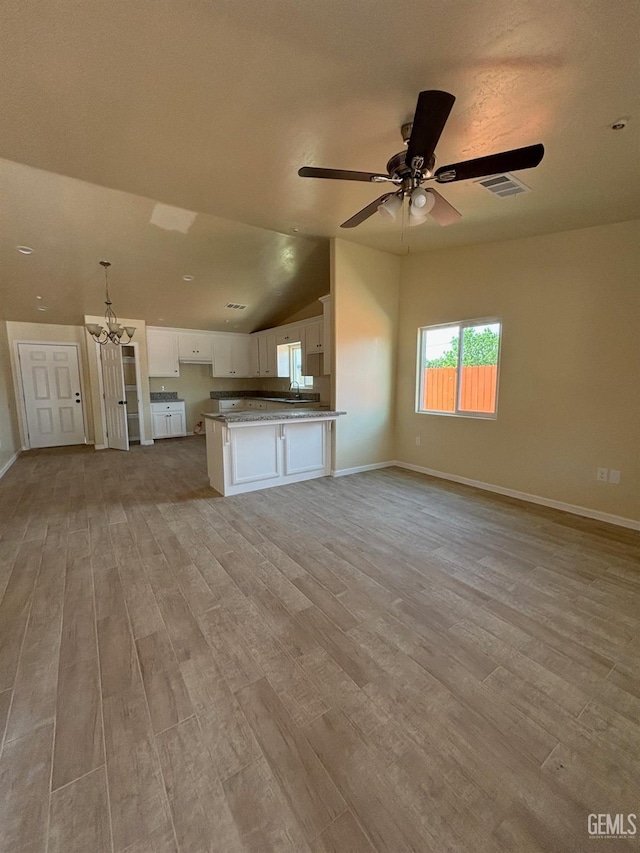 unfurnished living room featuring visible vents, baseboards, light wood finished floors, ceiling fan with notable chandelier, and vaulted ceiling