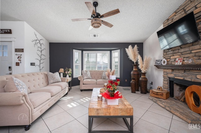 tiled living room featuring ceiling fan, a stone fireplace, and a textured ceiling