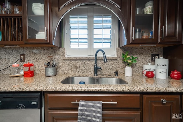 kitchen with dark brown cabinetry, sink, light stone counters, stainless steel dishwasher, and decorative backsplash