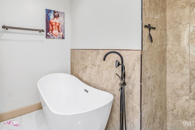 bathroom featuring a soaking tub, marble finish floor, and tile walls