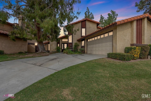 view of front of house featuring a garage, a tile roof, driveway, a lawn, and stucco siding