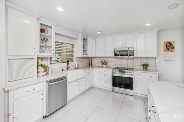 kitchen featuring stainless steel appliances, a sink, white cabinetry, marble finish floor, and glass insert cabinets