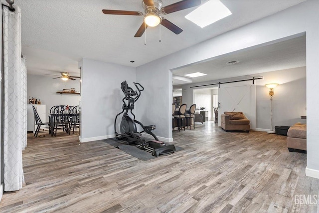 exercise area with hardwood / wood-style floors, a barn door, a textured ceiling, and ceiling fan