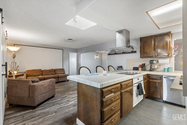 kitchen featuring dishwasher, tile counters, decorative backsplash, exhaust hood, and kitchen peninsula