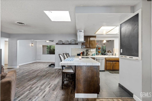 kitchen with ceiling fan, dishwasher, tile counters, a kitchen bar, and kitchen peninsula