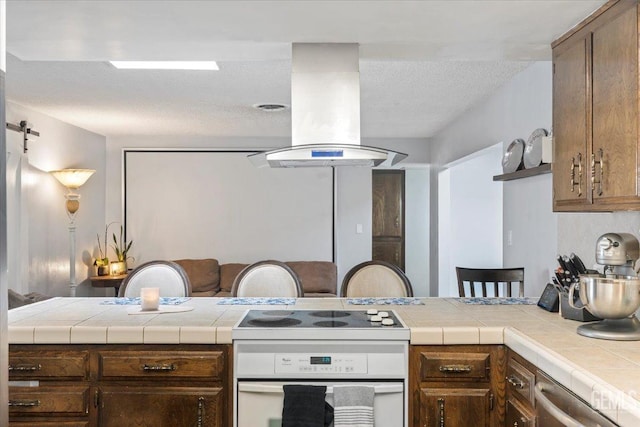 kitchen with electric range, tile counters, a barn door, and island exhaust hood