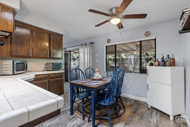 kitchen with dark brown cabinetry, tile countertops, dark hardwood / wood-style floors, ceiling fan, and backsplash