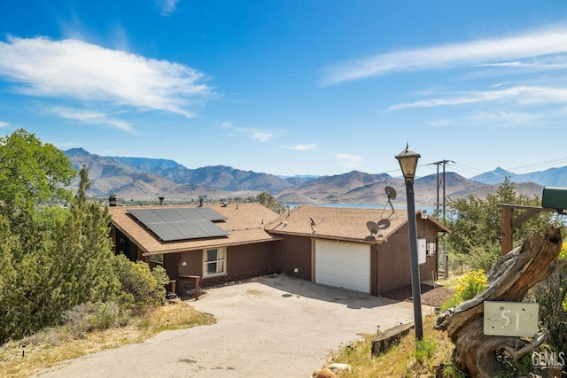 view of front of house with dirt driveway, a mountain view, a garage, solar panels, and roof with shingles