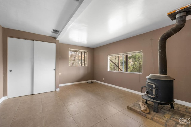 unfurnished living room with a wood stove, tile patterned floors, baseboards, and visible vents