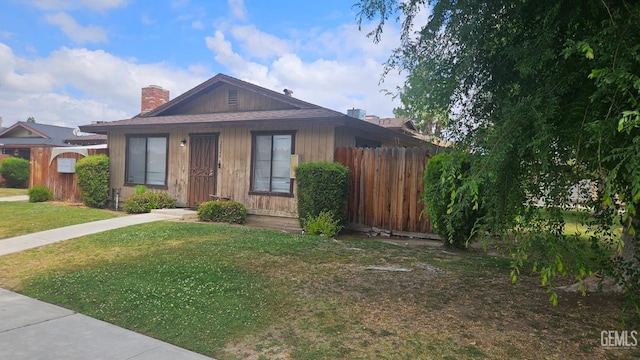 bungalow-style home with fence, a chimney, and a front lawn