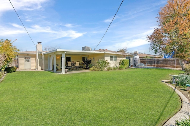 back of house featuring fence, a patio area, a lawn, and a chimney