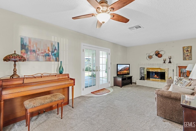 carpeted living room with visible vents, a textured ceiling, a brick fireplace, and ceiling fan