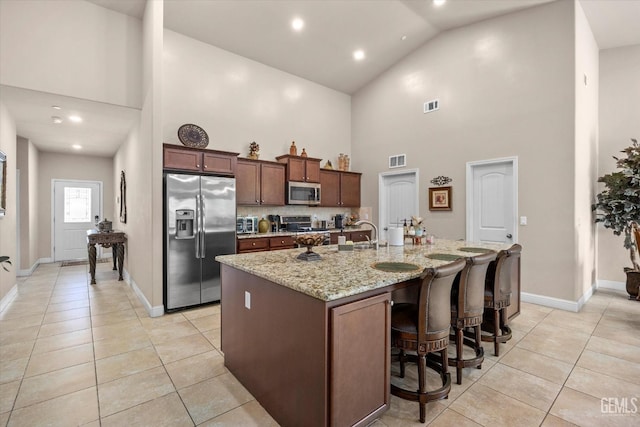 kitchen with stainless steel appliances, high vaulted ceiling, light tile patterned floors, a center island with sink, and baseboards