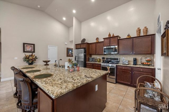 kitchen with appliances with stainless steel finishes, light tile patterned floors, tasteful backsplash, a kitchen bar, and light stone counters