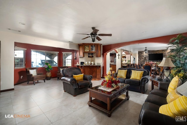 living area featuring light tile patterned floors, visible vents, arched walkways, and ceiling fan