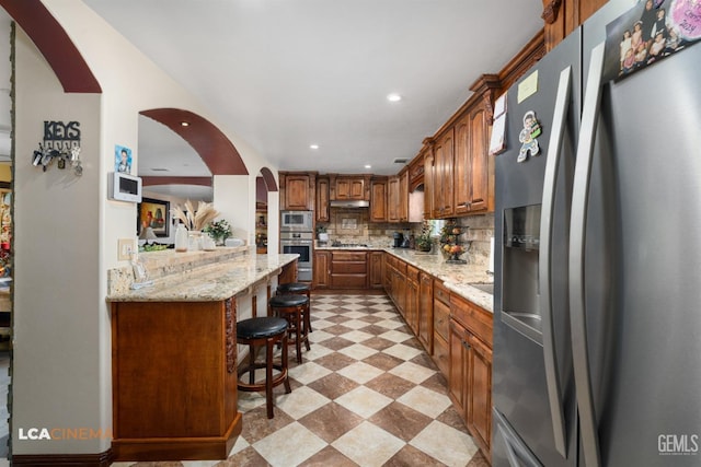 kitchen with tasteful backsplash, a kitchen bar, light floors, stainless steel appliances, and arched walkways