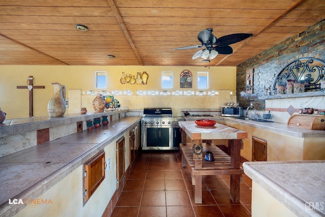 kitchen with stainless steel microwave, a ceiling fan, wood ceiling, and dark tile patterned flooring