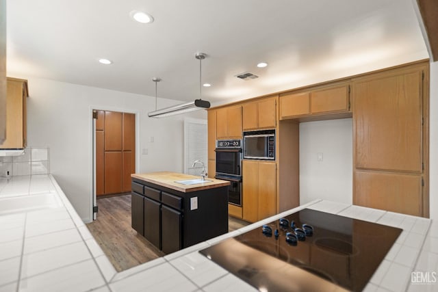 7108 Luke Ave, Bakersfield, CA 93308 - kitchen featuring black appliances, a sink, tile counters, an island with sink, and light wood-style floors