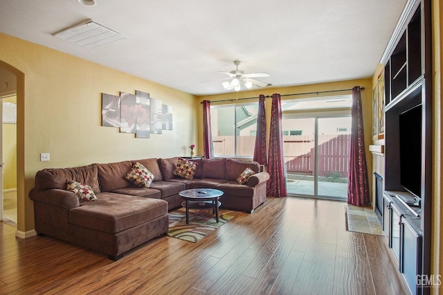 living room featuring arched walkways, visible vents, wood finished floors, and a ceiling fan