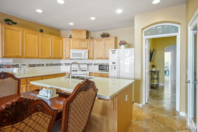 kitchen featuring white appliances, arched walkways, light countertops, light brown cabinets, and a sink