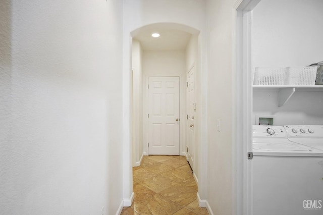 hallway with arched walkways, baseboards, and separate washer and dryer