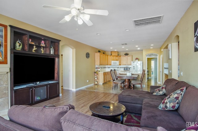 living room featuring arched walkways, recessed lighting, a ceiling fan, visible vents, and light wood-style floors