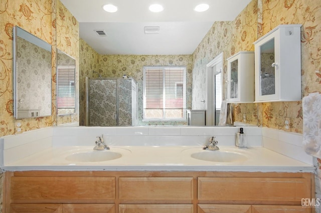 full bathroom with double vanity, a stall shower, a sink, and wallpapered walls