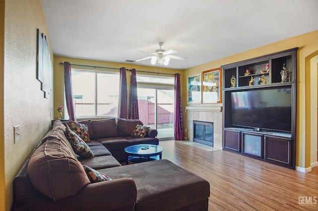 living room featuring visible vents, baseboards, a tiled fireplace, ceiling fan, and light wood-type flooring