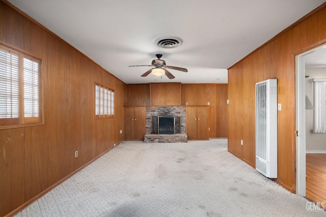 unfurnished living room with ceiling fan, wood walls, light colored carpet, and a fireplace