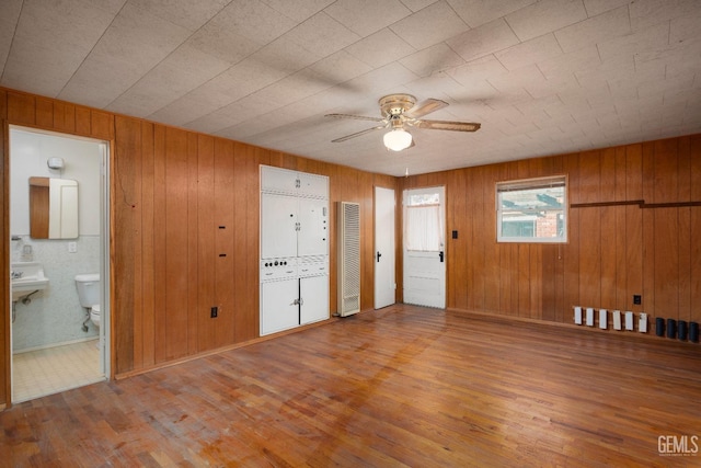 unfurnished room with hardwood / wood-style floors, ceiling fan, wood walls, and sink