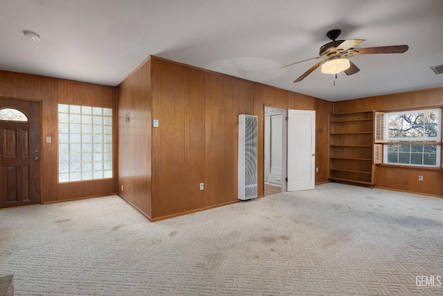 interior space featuring light colored carpet, ceiling fan, and wooden walls