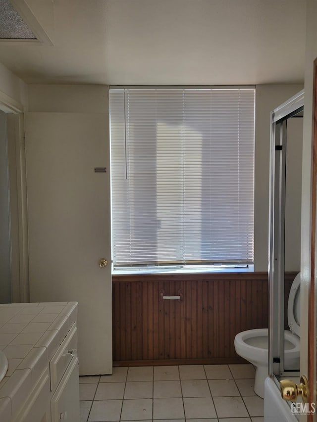 bathroom with toilet, vanity, tile patterned floors, wooden walls, and a shower with shower door