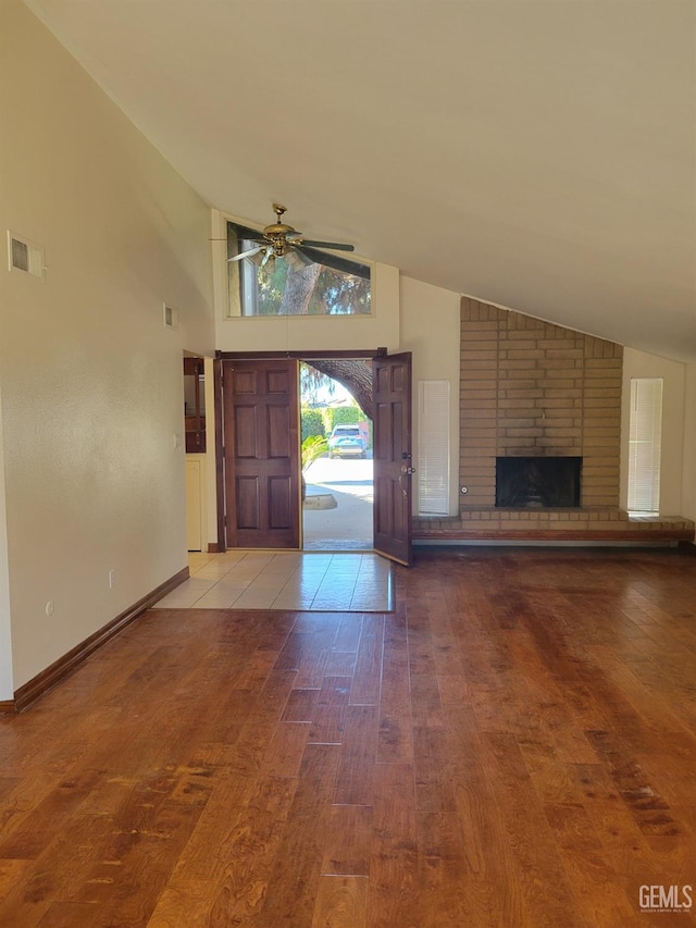 foyer with hardwood / wood-style floors, a brick fireplace, a towering ceiling, and ceiling fan