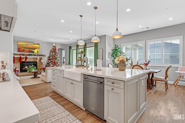 kitchen with sink, dishwasher, light hardwood / wood-style flooring, decorative light fixtures, and a center island with sink