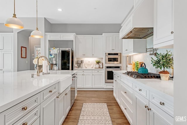 kitchen with backsplash, pendant lighting, white cabinets, custom exhaust hood, and appliances with stainless steel finishes