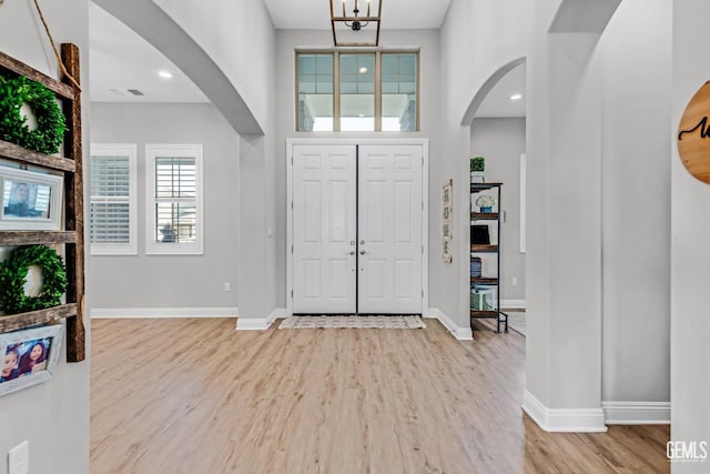 entryway featuring a notable chandelier, a towering ceiling, and light hardwood / wood-style flooring