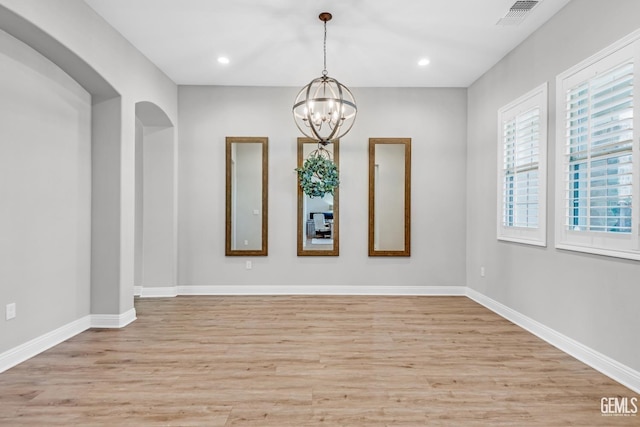 spare room featuring light hardwood / wood-style floors, a healthy amount of sunlight, and a notable chandelier