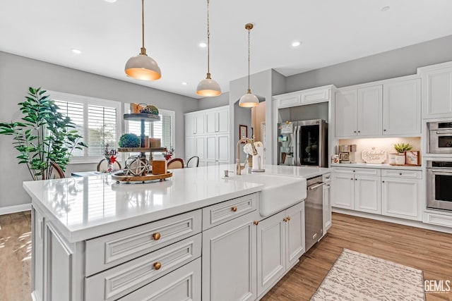 kitchen featuring stainless steel fridge, pendant lighting, light hardwood / wood-style floors, a kitchen island with sink, and white cabinets