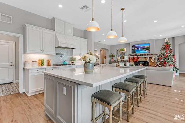 kitchen with a breakfast bar area, white cabinets, hanging light fixtures, and custom range hood