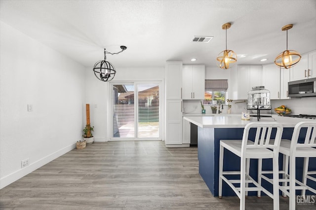 21633 Golden Hills Blvd, Tehachapi, CA 93561 - kitchen with stainless steel microwave, light countertops, white cabinetry, hanging light fixtures, and a breakfast bar area