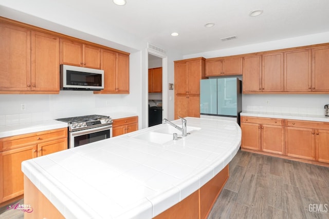 kitchen with appliances with stainless steel finishes, a kitchen island with sink, tile counters, and sink