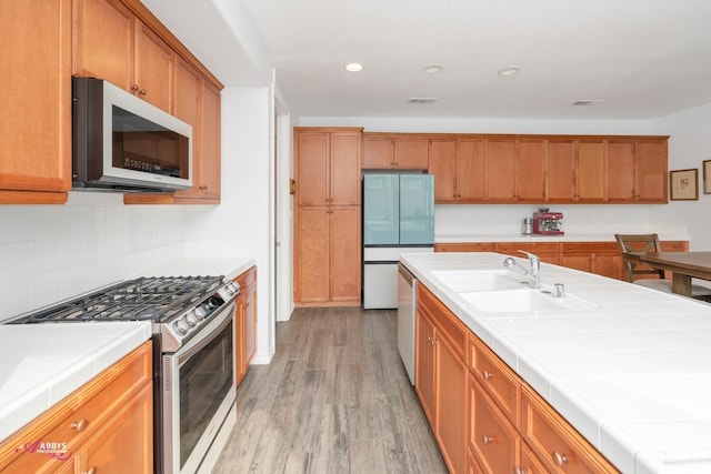 kitchen featuring appliances with stainless steel finishes, light wood-type flooring, tile countertops, and sink