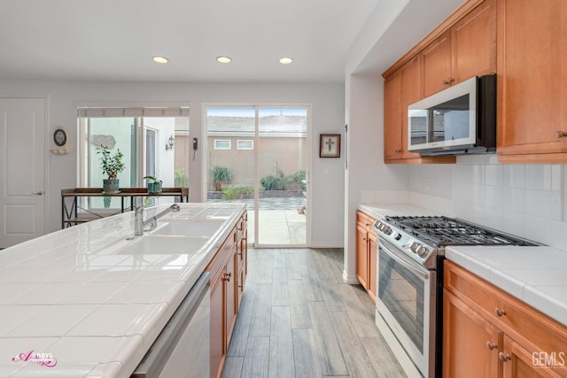 kitchen featuring dishwashing machine, gas range, sink, tile countertops, and light hardwood / wood-style flooring