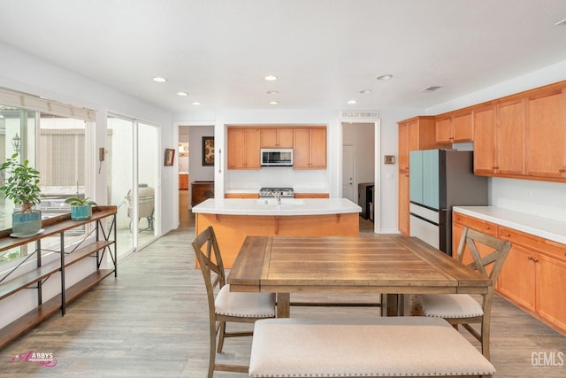 kitchen featuring decorative backsplash, light hardwood / wood-style flooring, an island with sink, and appliances with stainless steel finishes