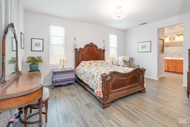 bedroom with ensuite bathroom, multiple windows, and light hardwood / wood-style flooring