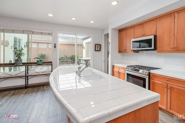 kitchen with tile counters, a center island, sink, and stainless steel gas range