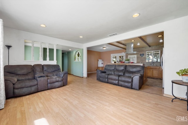 living area featuring recessed lighting, beam ceiling, visible vents, and light wood finished floors